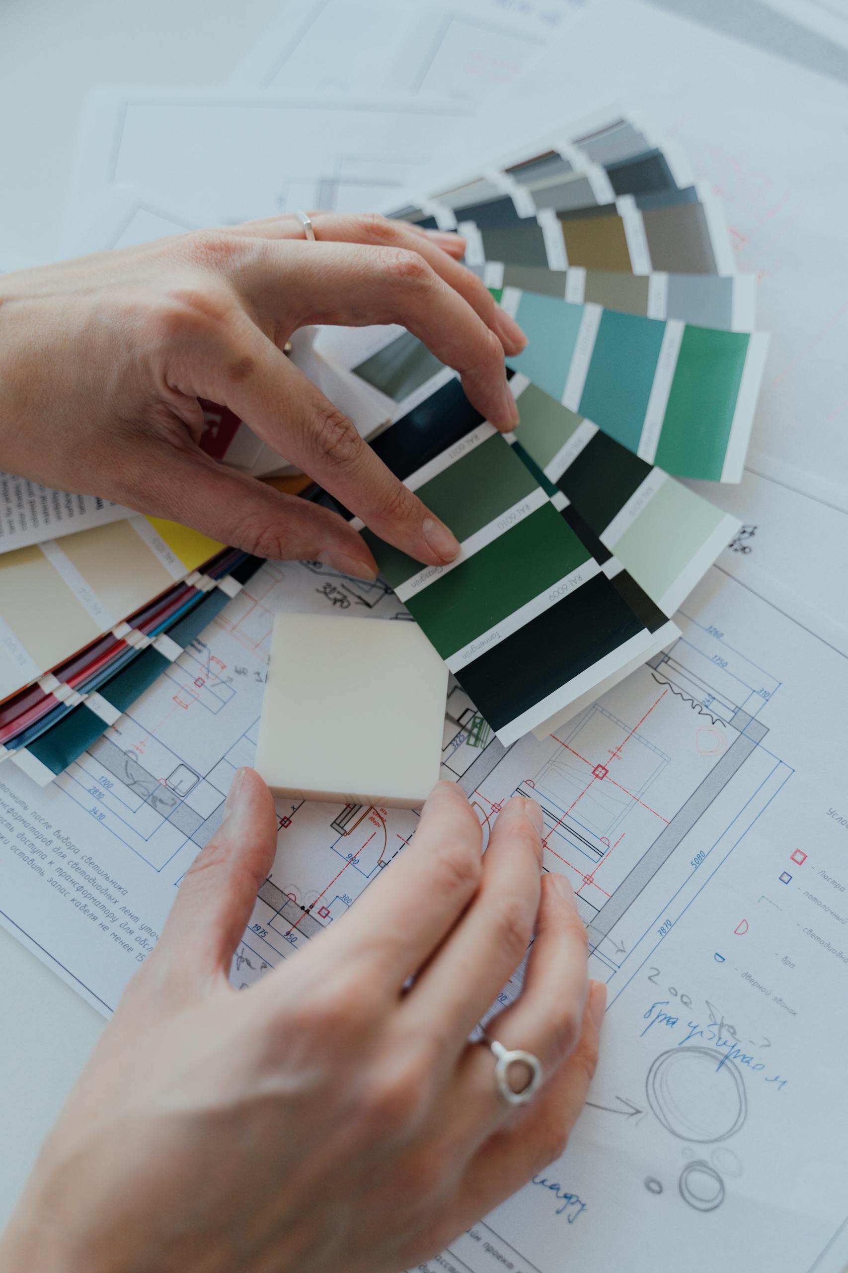 Hands selecting color samples over architectural plans for interior design.